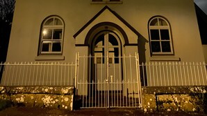 A building with a triangular roof, two illuminated windows, and a gated entrance. - Formerly, Zoar Congregational Chapel offering a unique stay in Pembrokeshire  (Kilgetty)