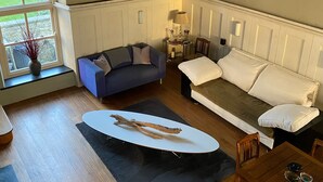 A spacious living room with a large window, a blue sofa, a white sofa, a dining table, and a wooden floor. - Formerly, Zoar Congregational Chapel offering a unique stay in Pembrokeshire  (Kilgetty)