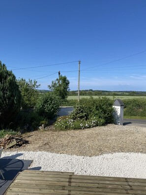 A gravel driveway leading to a wooden deck with a metal chair.