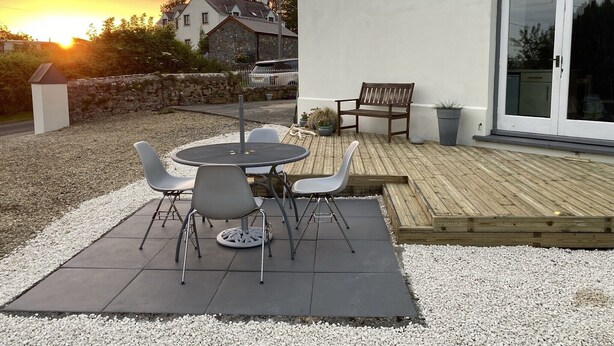 A patio with a round table and chairs, a wooden deck, and a white building with large windows. - Formerly, Zoar Congregational Chapel offering a unique stay in Pembrokeshire  (Kilgetty)