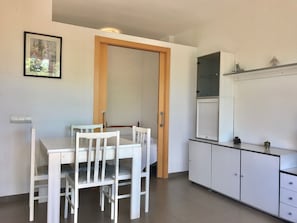 A small, clean kitchen with white cabinets, a dining table, and chairs.