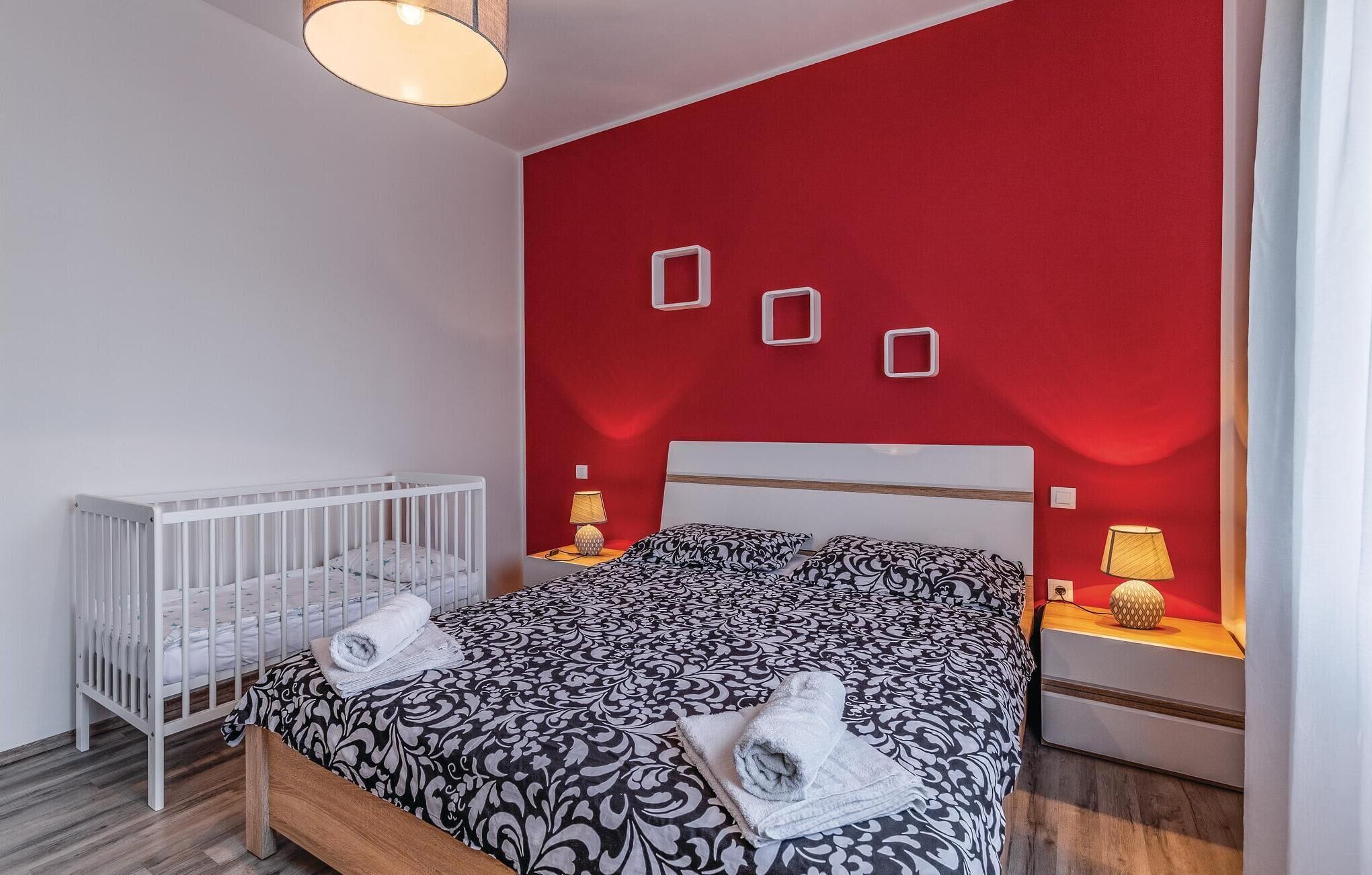 Una stanza con una culla, un letto con biancheria a motivi e una parete decorata di rosso.