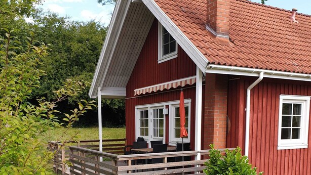 Une maison en bois rouge avec un porche blanc, une cheminée et un petit jardin.