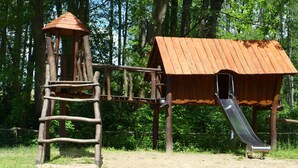 Une structure de jeux en bois, dotée d’un toboggan et d’une zone d’escalade, entourée d’arbres.
