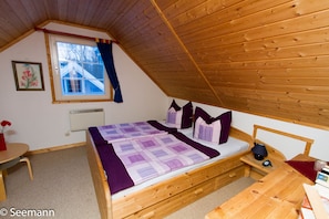 Cozy single-room accommodation with a wooden bed, small table, and chair, set amidst exposed wooden beams.