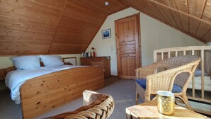 Une chambre mansardée chaleureuse, avec un lit en bois, une chaise en osier, une petite table et une porte.