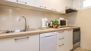 Uma cozinha moderna com armários brancos, uma pia de aço inoxidável, cafeteira, micro-ondas e lava-louças.