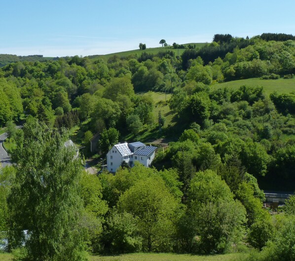 Une maison dotée de panneaux solaires, entourée d’une végétation luxuriante et de collines verdoyantes.