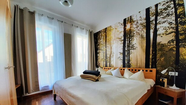 Une chambre d’hôtel avec un grand lit, une table de chevet et une fresque murale sur le thème de la forêt.