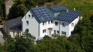 Une maison à deux étages, dotée de panneaux solaires sur le toit et entourée d’arbres.