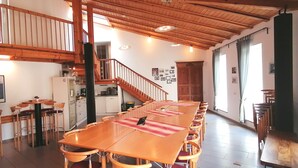 Un vaste espace dédié à la salle à manger, avec une longue table et des chaises en bois, une cuisine à l’arrière-plan et un escalier menant à un niveau supérieur.