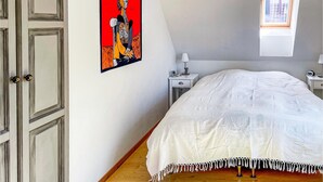 Ein Schlafzimmer mit Bett, Nachttisch, Lampe, einem Gemälde und einem Fenster.
