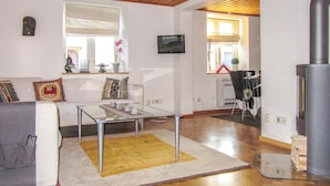 Ein Wohnzimmer mit einem Glastisch, einer Couch mit gemusterten Kissen, einem gelben Teppich, einem Kamin und einem an der Wand befestigten Fernseher.