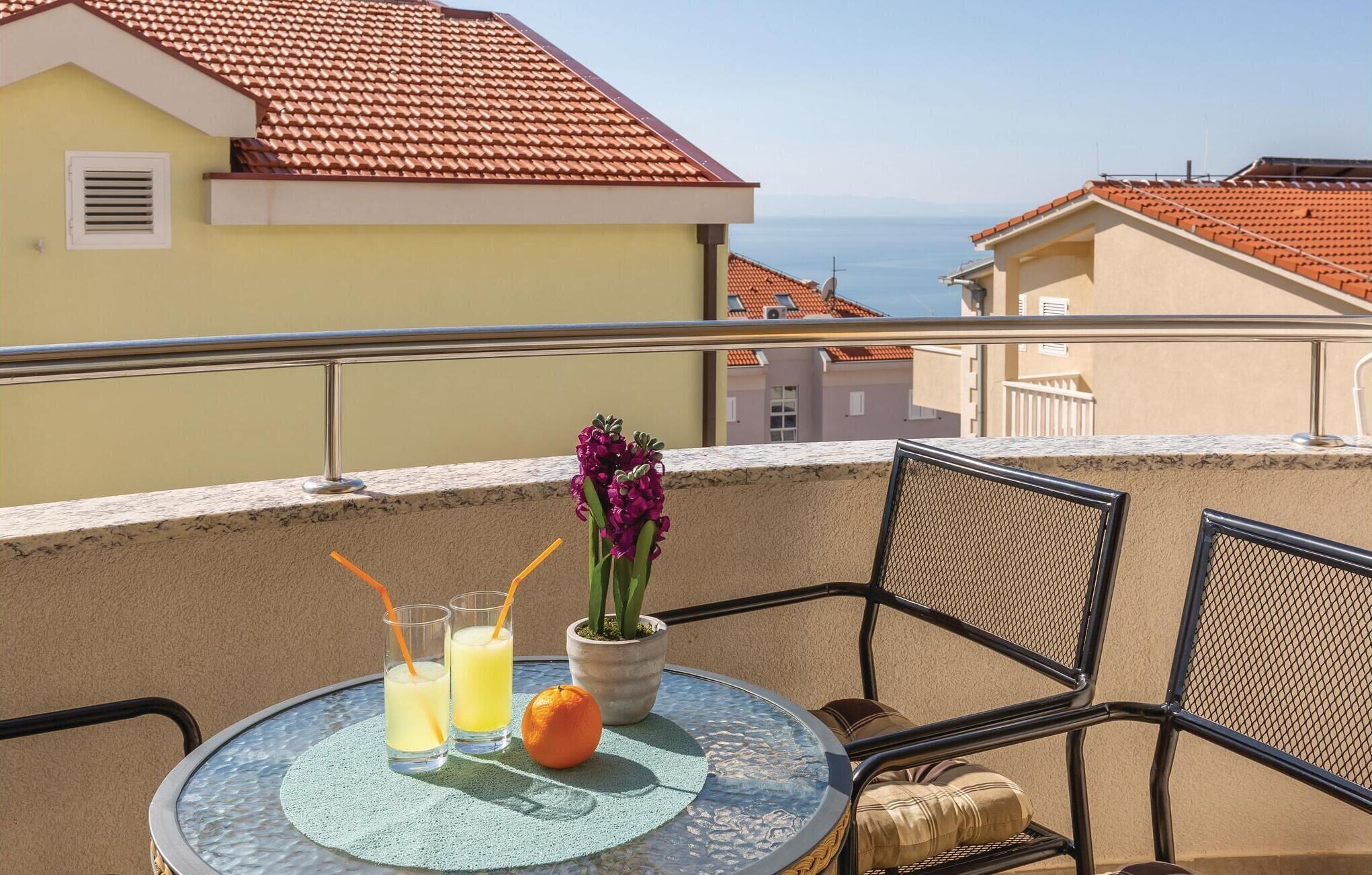 A balcony with a round table, two glasses of orange juice, a potted plant, and a chair.