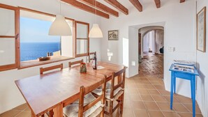 A dining area with a wooden table and chairs, a view of the sea through large windows, and a hallway leading to another room. - Vacation Home "Casa Can Sans" with Sea Views (BANYALBUFAR)