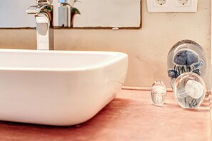A bathroom sink with a faucet, a mirror, and a clear glass container with a sponge.