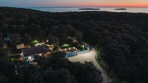 A secluded house surrounded by dense forest, with a clear view of the ocean at sunset.