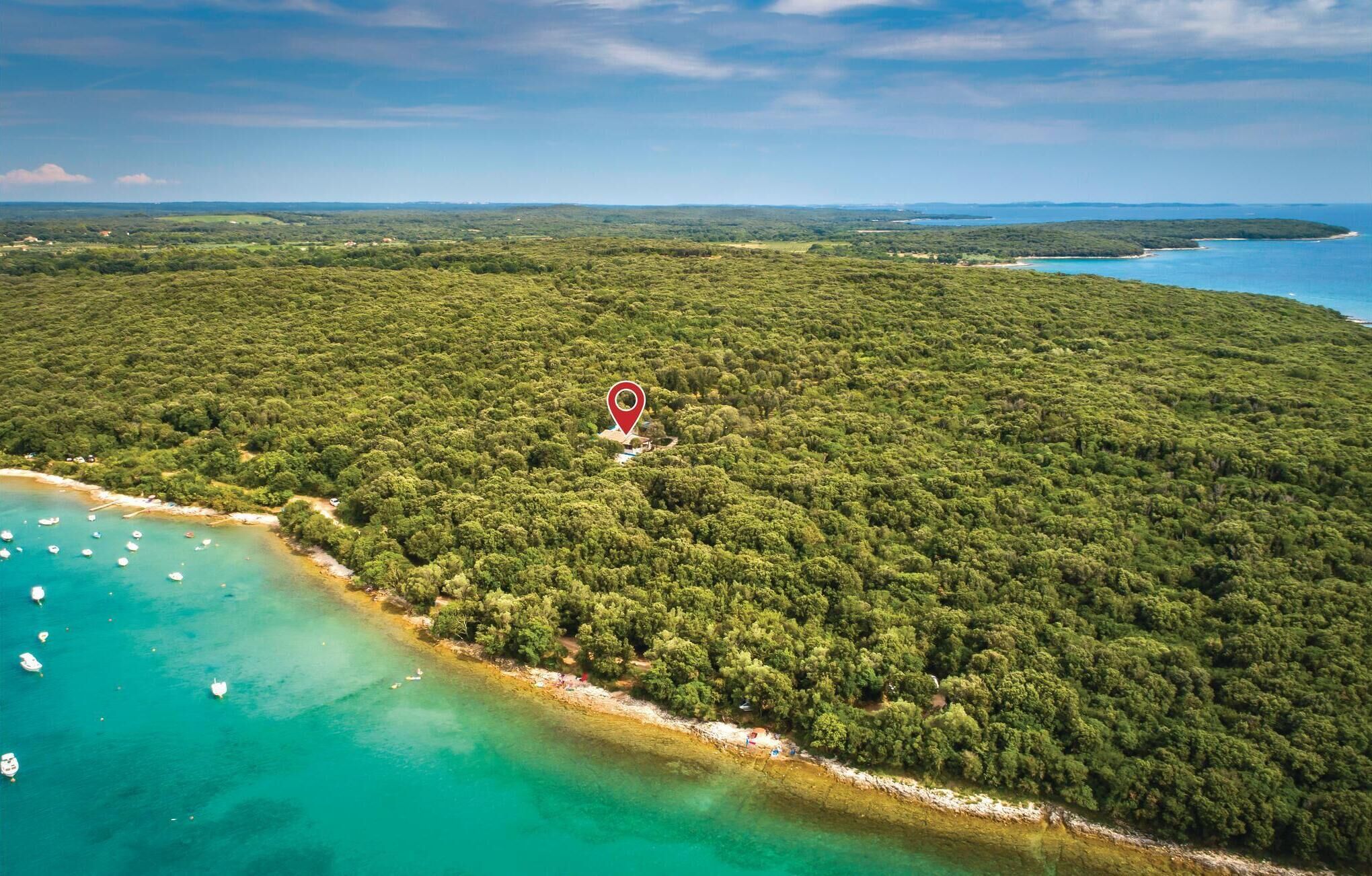 An aerial view of a coastal forested area with a clear beach and boats in the water.