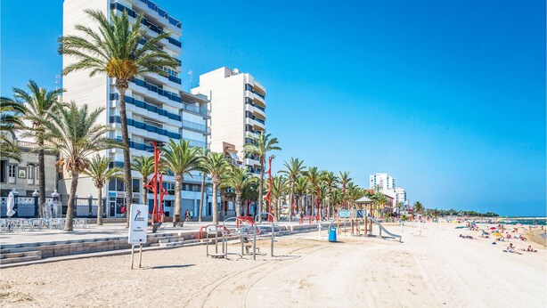 Een hotel aan het strand met meerdere verdiepingen, palmbomen en een zandstrand.