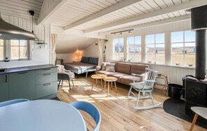 Un intérieur chaleureux comprenant une cuisine, un coin repas et un espace détente près de grandes fenêtres.