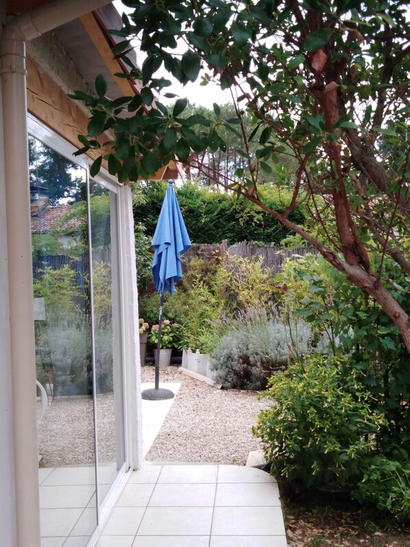 A patio area with a glass door leading to a garden. - Maisonette classified ***, in the heart of the greenery, between ocean and Landes forest (Saint-Julien-En-Born)