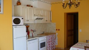 A compact kitchen with white appliances, a microwave, a dishwasher, and a stove. There is a wooden cabinet above the sink, and a chandelier hangs from the ceiling.