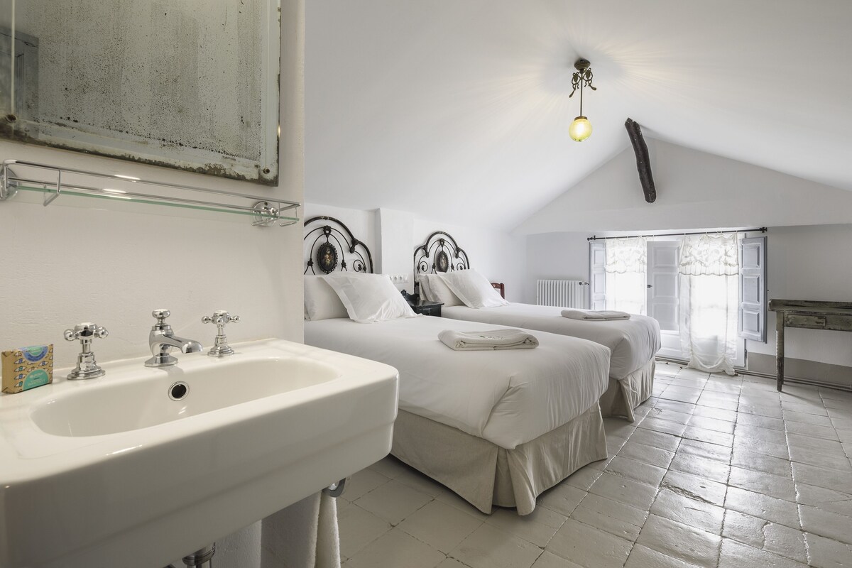 Un dormitorio con dos camas, un espejo grande, un lavamanos y una ventana con cortinas.