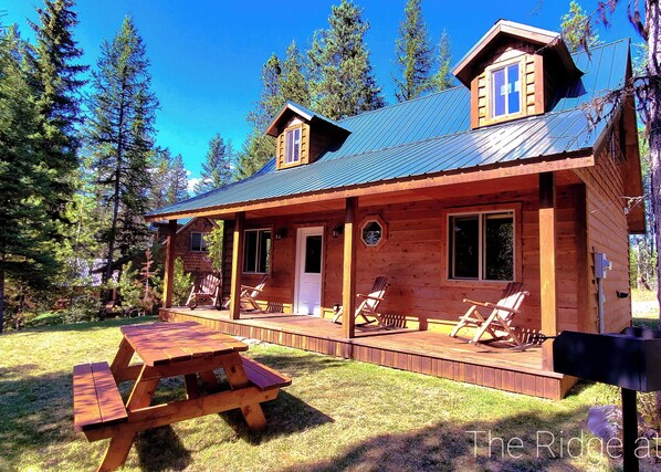 A wooden cabin with a covered porch, multiple windows, and a picnic table.