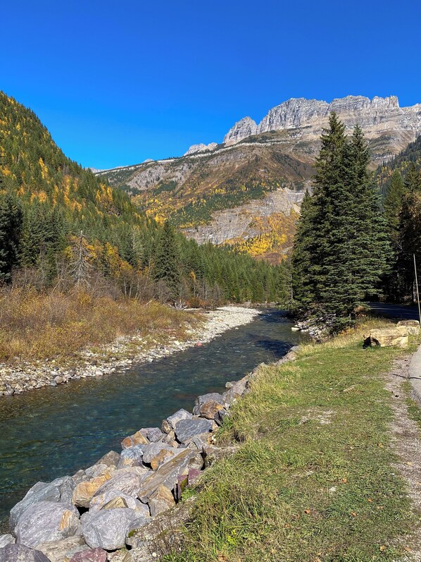 Ein klarer Fluss mit felsigen Ufern, umgeben von bewaldeten Hügeln und einer Bergkette im Hintergrund.