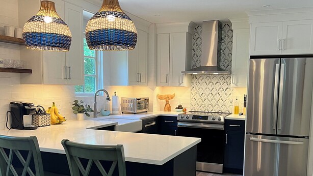 A modern kitchen with white cabinetry, a central island with bar stools, stainless steel appliances, and decorative blue and gold pendant lights. - The Perfect Location to relax and explore all that the Seacoast has to offer!  (Eliot)