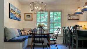 A dining area with a wooden table, black chairs, and a bench with cushions. There is a window with a view of greenery outside. - The Perfect Location to relax and explore all that the Seacoast has to offer!  (Eliot)