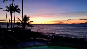 A poolside view at sunset with palm trees and a view of the ocean.