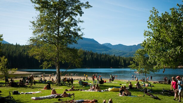 A lakeside park with people relaxing on grass, boats, and bicycles. - Spacious Rustic Whistler Retreat at the Woods (Whistler)