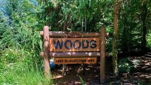 A wooden sign with the word "WOODS" and an address "4652 BLACKCOMB WAY" in a forested area. - Spacious Rustic Whistler Retreat at the Woods (Whistler)