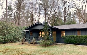 A dark-colored cabin with a porch, surrounded by trees and a grassy yard. - IN TOWN! 2 Blocks From Main Street. 2 Bedrooms/2 Baths. Free WiFi. Sleeps 4.  (Highlands)