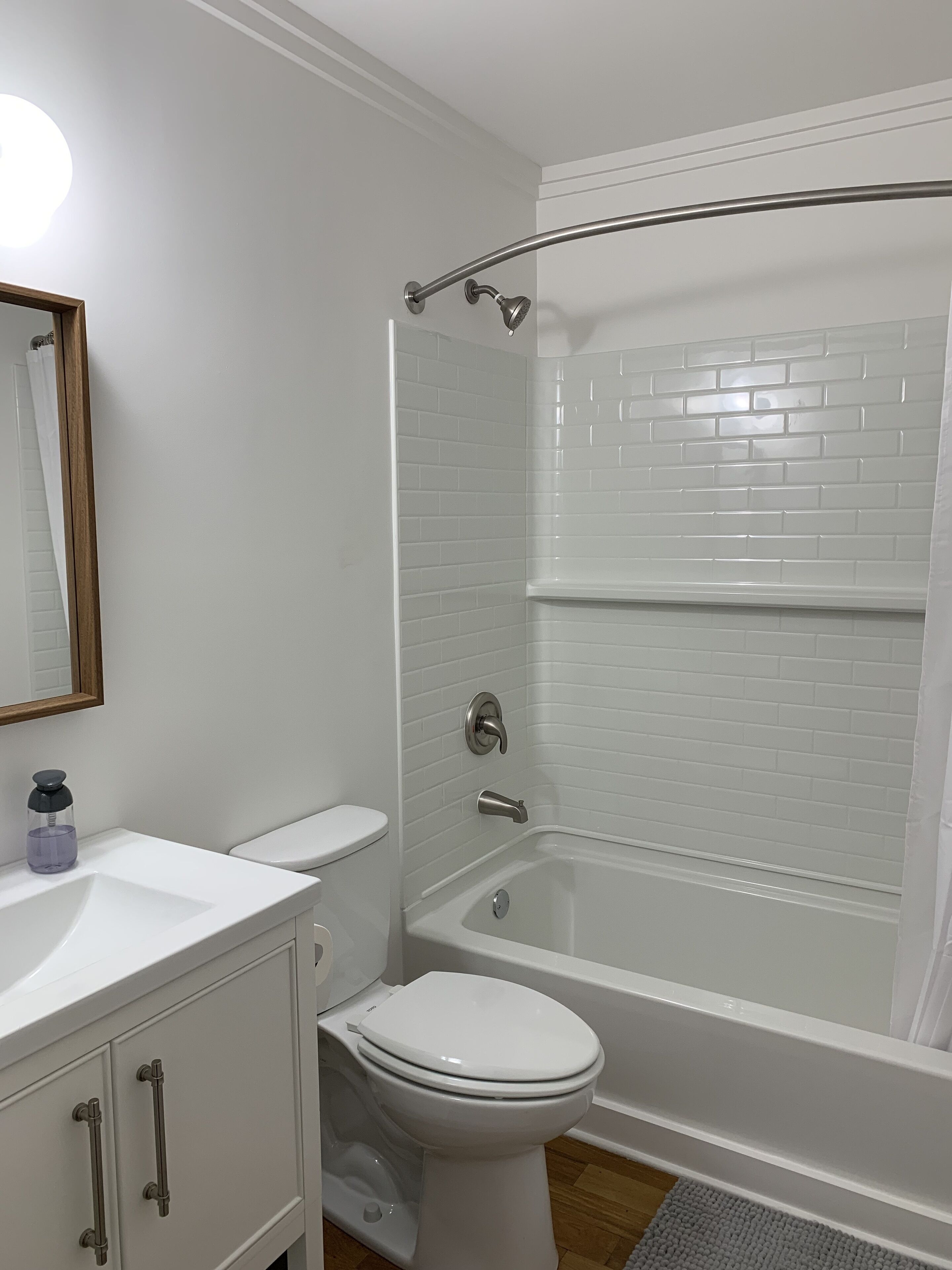 Een badkamer met een wit toilet, een wastafel met zeepdispenser, een bad met douchegordijn, en een spiegel aan de muur.