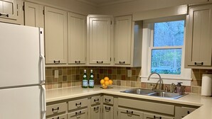 Una cocina con armarios blancos, encimera de granito, estufa integrada y ventana con vistas a árboles.