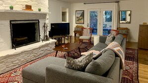 Una sala de estar con chimenea, un sofá, un televisor y vistas al exterior a través de un ventanal.