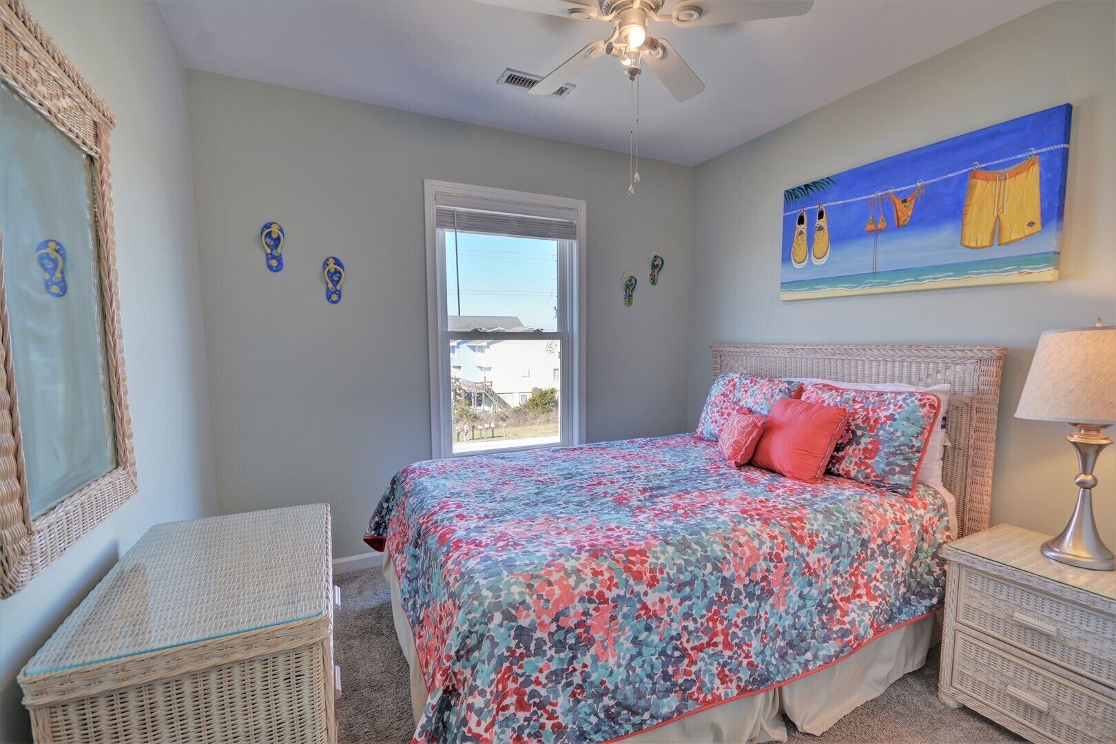 A bedroom with a bed, a nightstand, a wicker chair, a ceiling fan, and a window.