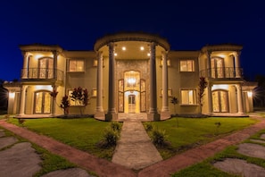 A grand mansion with a central entrance, large columns, and a well-lit facade. - Oceanfront Vacation Rental (Hakalau)
