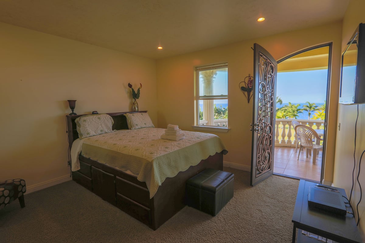 A bedroom with a bed, a window, a balcony, and a desk with a computer.