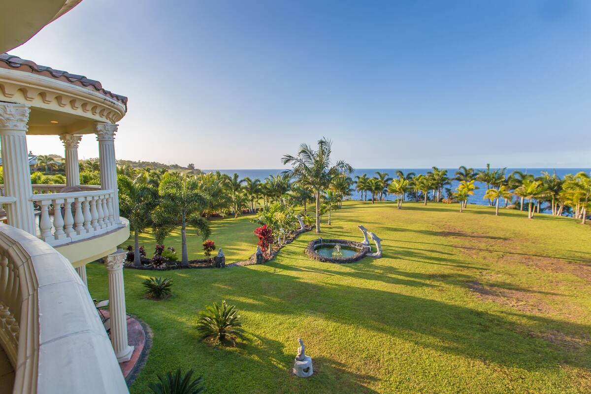 A well-maintained lawn with a gazebo, palm trees, and a small pond.