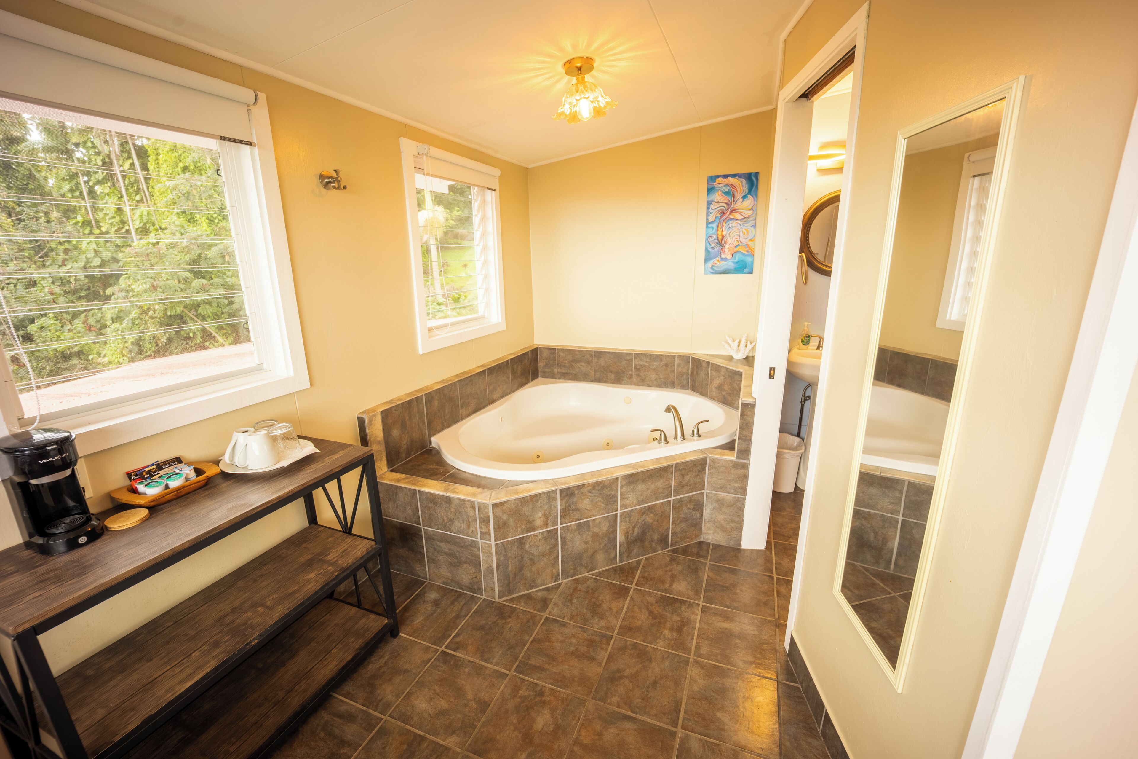 A bathroom with a bathtub, a window, a sink, and a coffee maker on a table.