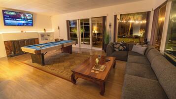 A living room with a pool table, a sofa, a coffee table, and a TV mounted on the wall.