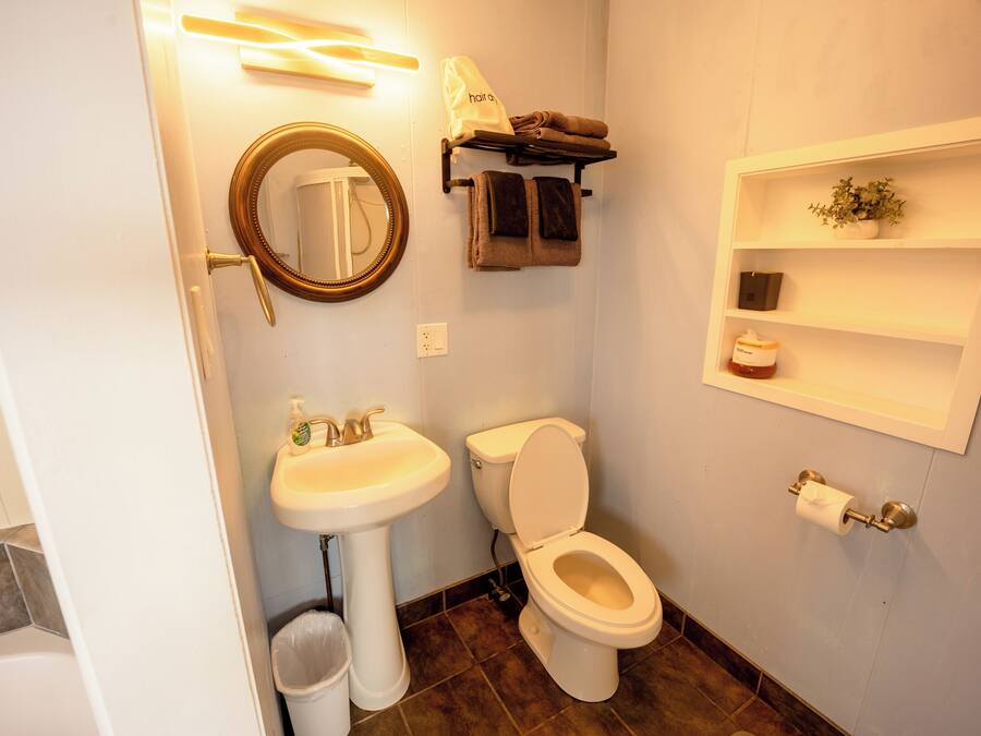 A bathroom with a sink, toilet, mirror, towel rack, and a shelf with toiletries.