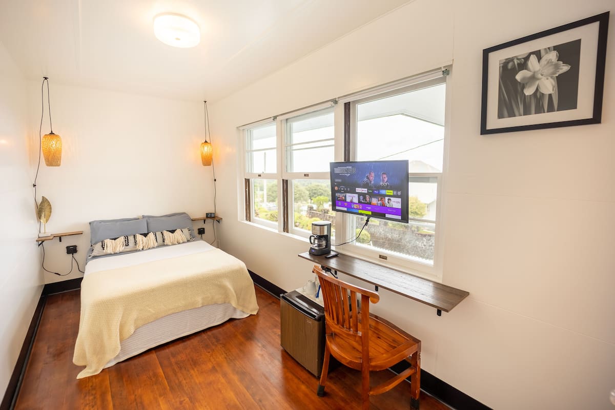 A bedroom with a bed, a desk with a computer, a chair, a coffee maker, and a window with a view.