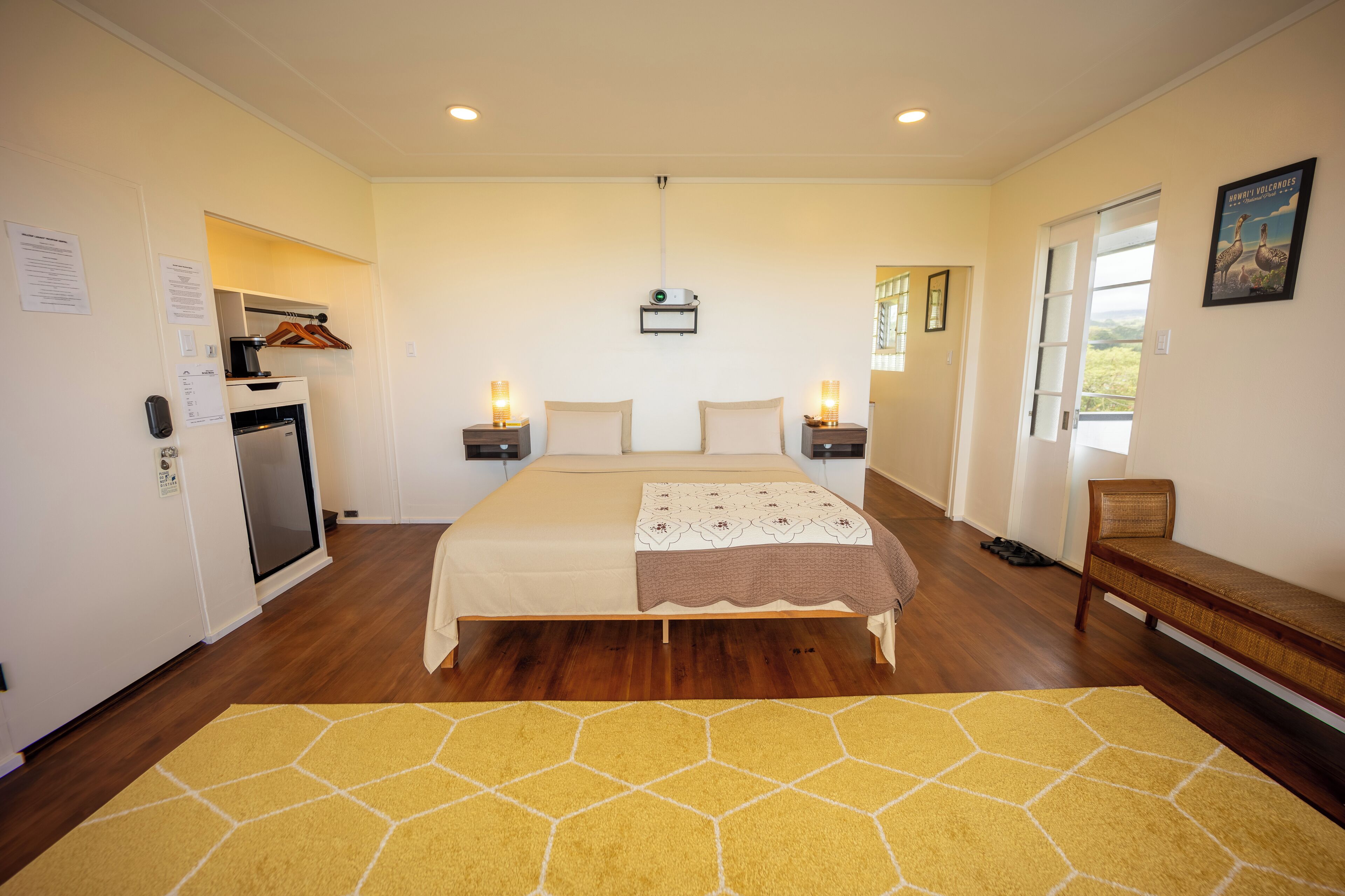 A bedroom with a bed, bedside tables, a bench, a desk, and a window.