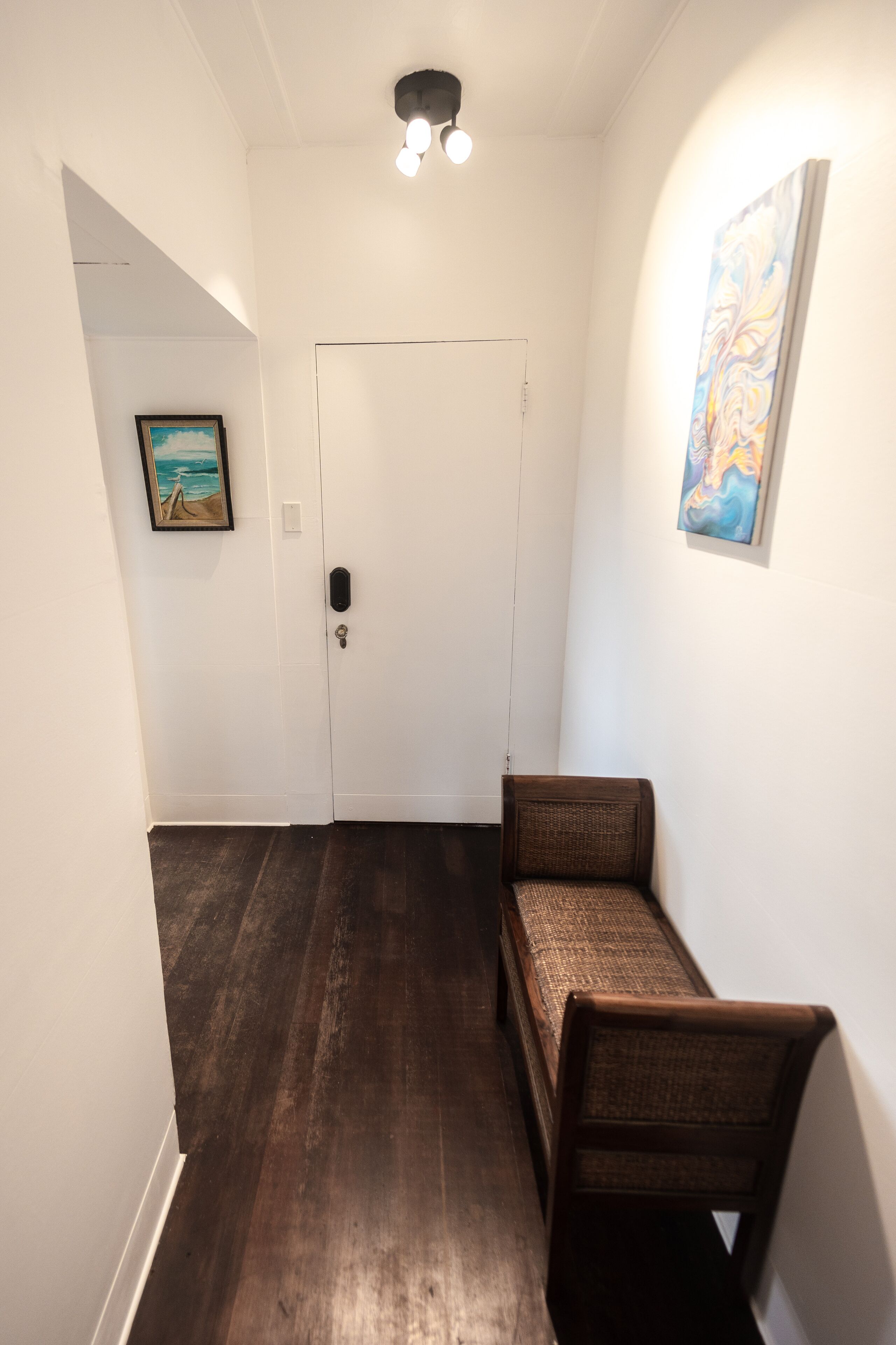Un pasillo con una puerta blanca, un banco y un cuadro en la pared.
