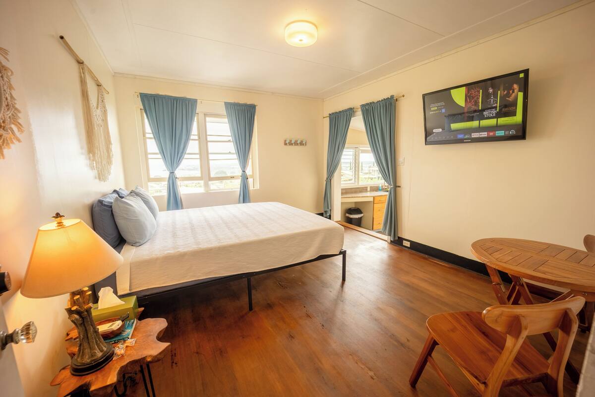 A room with a bed, a table, a chair, a lamp, and a television on the wall.