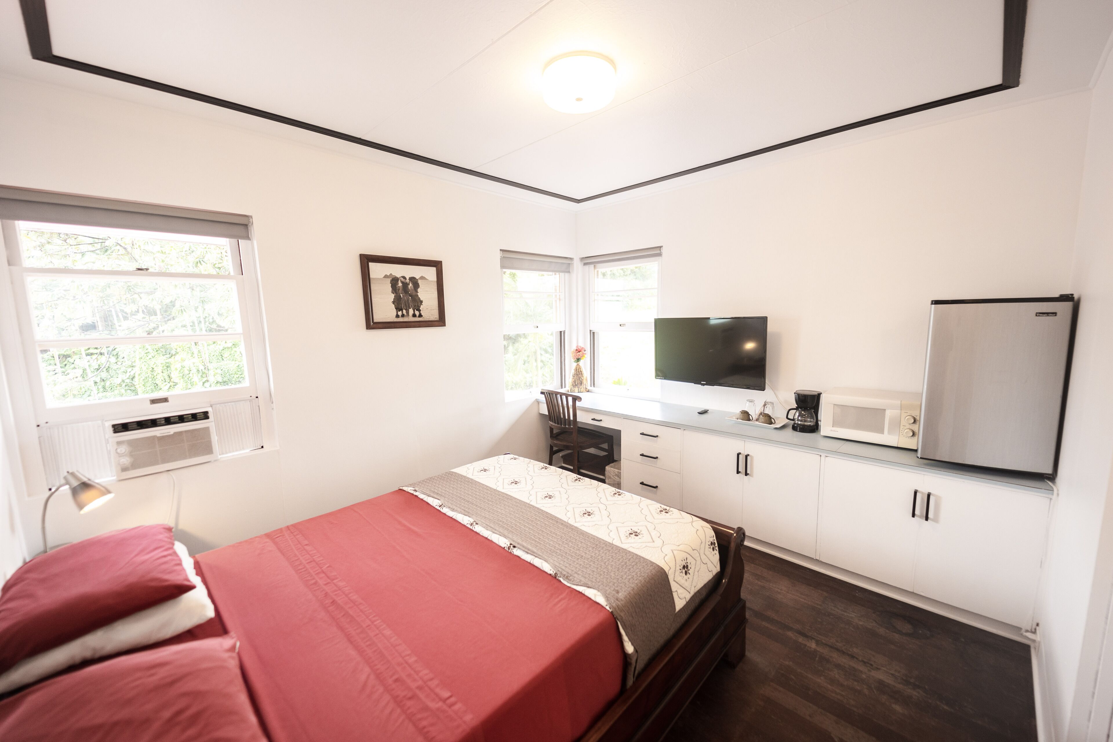 A bedroom with a bed, a desk, a chair, a television, a refrigerator, and a microwave.